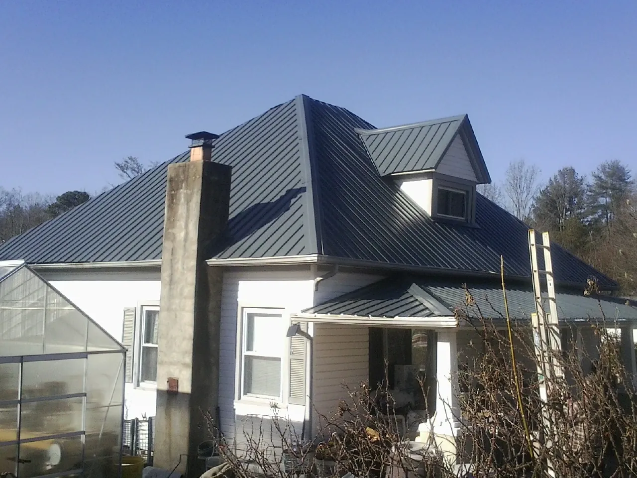 Dark blue standing seam metal roof on a white farmhouse with dormer — Slate & Tile Roof Repair by Roofing Brothers in East Marion