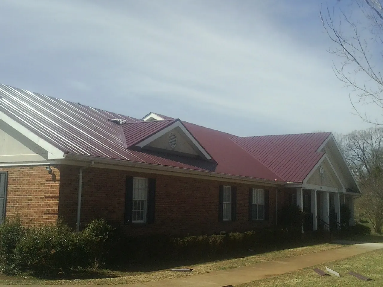 Red metal roof with gabled entries on a long brick building, from a Hail Damage Roof Repair job in East Marion