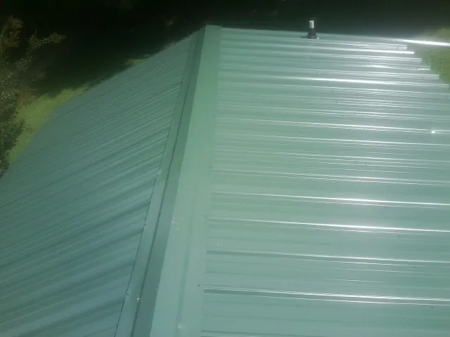 New green metal panels meeting at the ridge of a roof — Flat Roof Repair work by our crew in East Marion