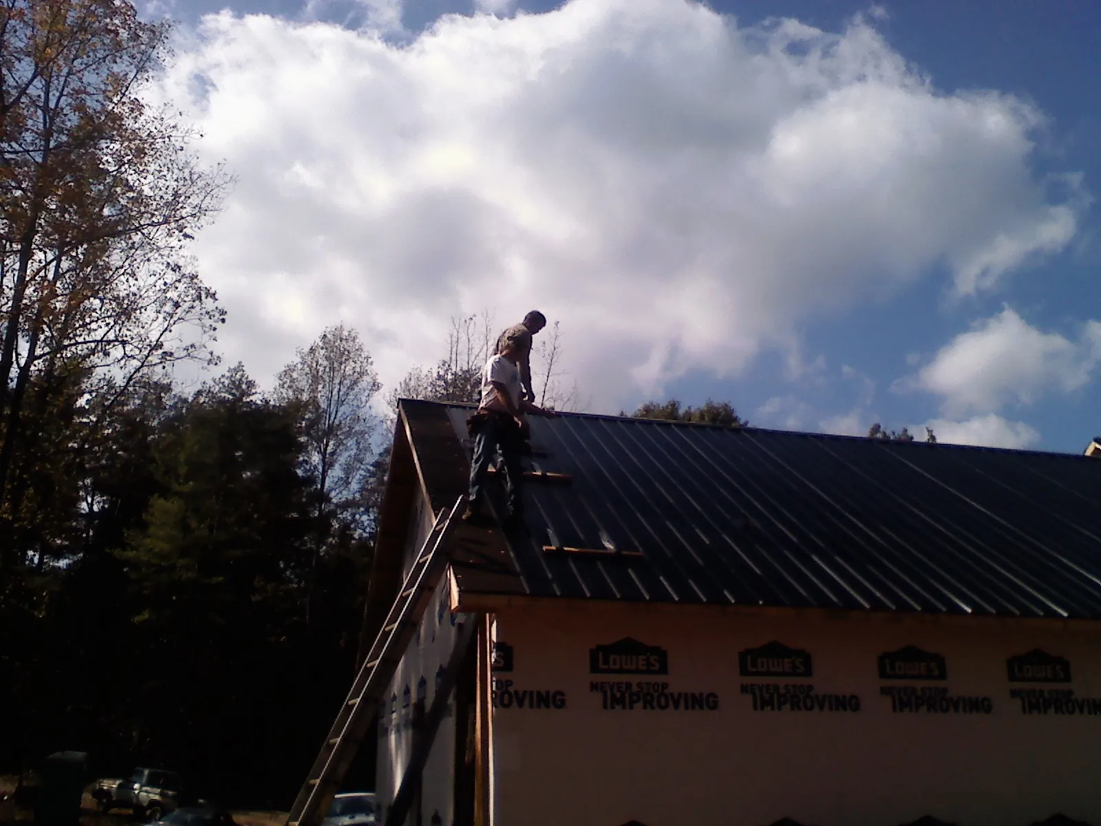 Roofer fastening dark metal panels high against a cloudy sky, from a Roof Inspection job in East Marion