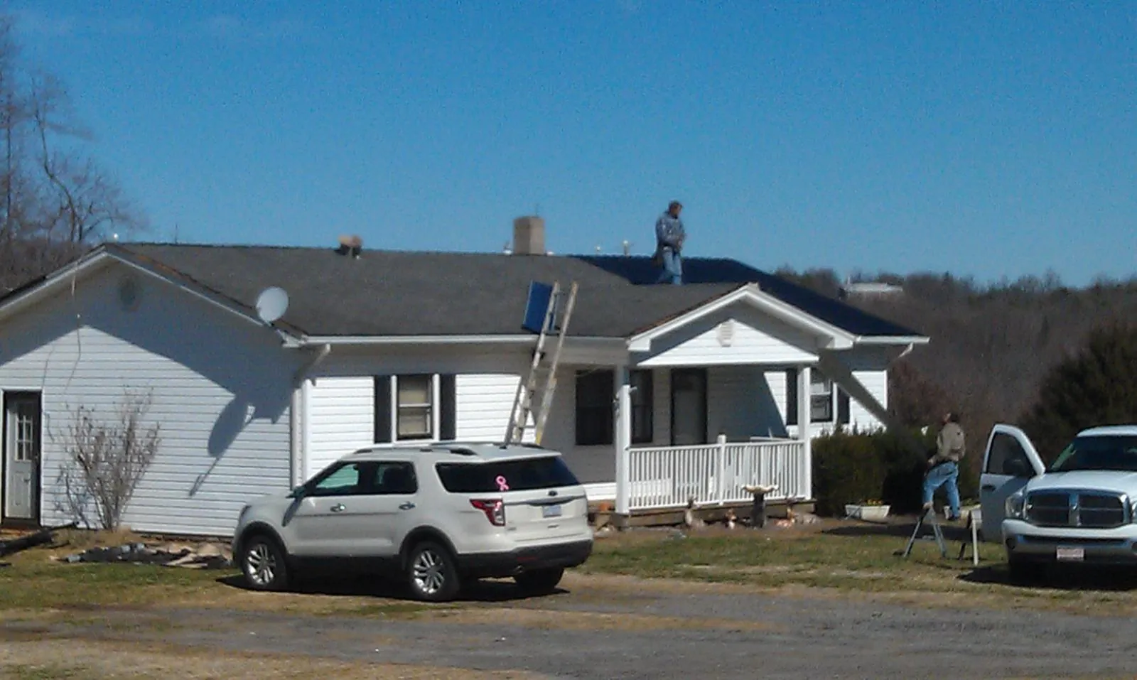 Roofers stripping shingles from a white ranch house roof in East Marion