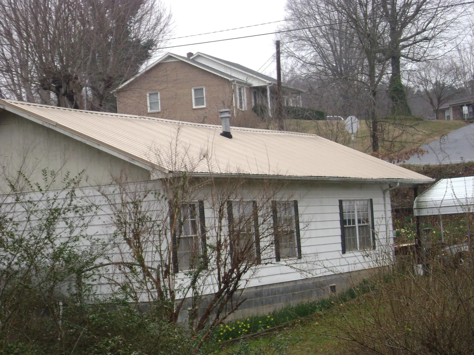 Tan metal roof on a white sided house set into a hillside — Commercial Roofing by Roofing Brothers in East Marion
